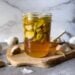 A pint jar full of garlic cloves and honey is sitting on top of a small wood cutting board. Bulbs and cloves of garlic surround the area.