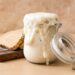 A jar with a flip top lid is overflowing with sourdough starter. Just beyond is a wood cutting board with two slices of bread.