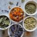 White ceramic bowls are filled with a variety of dried herbs including basil, lavender, calendula, and chamomile.