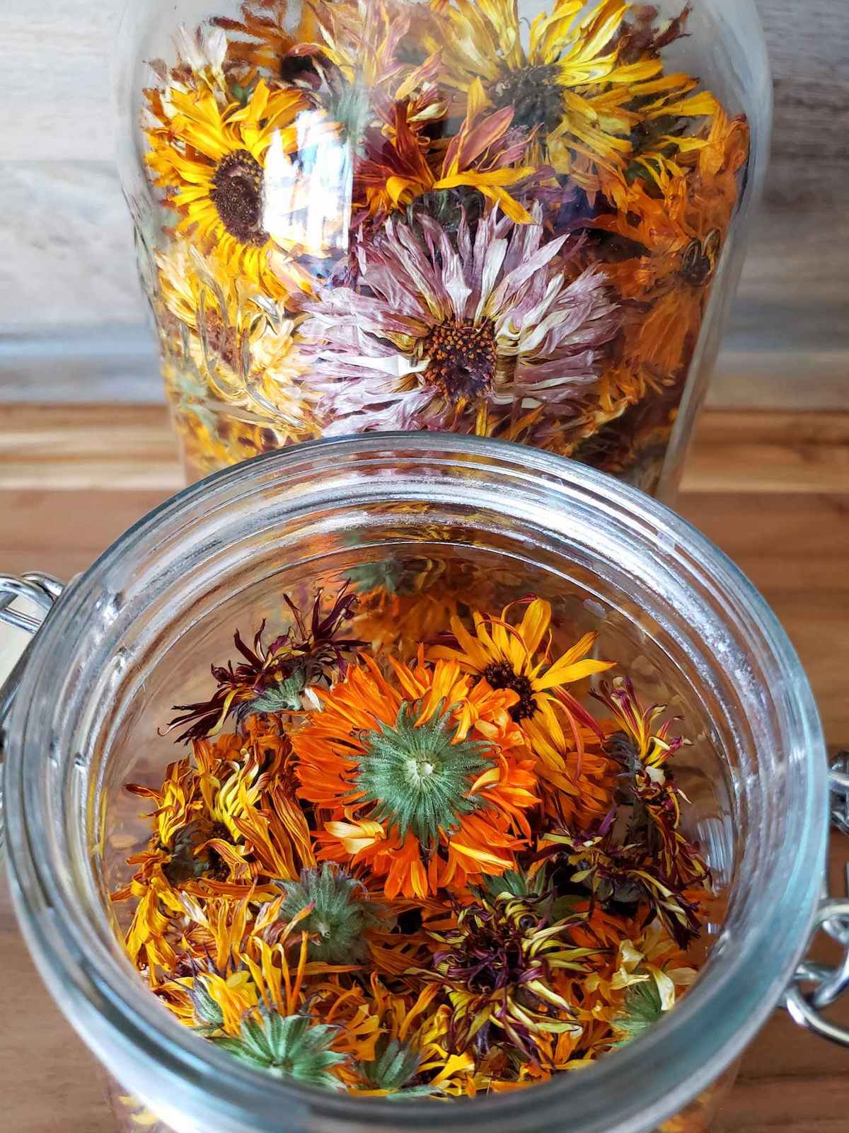 Two glass jars are full of dried calendula flowers of various colors.