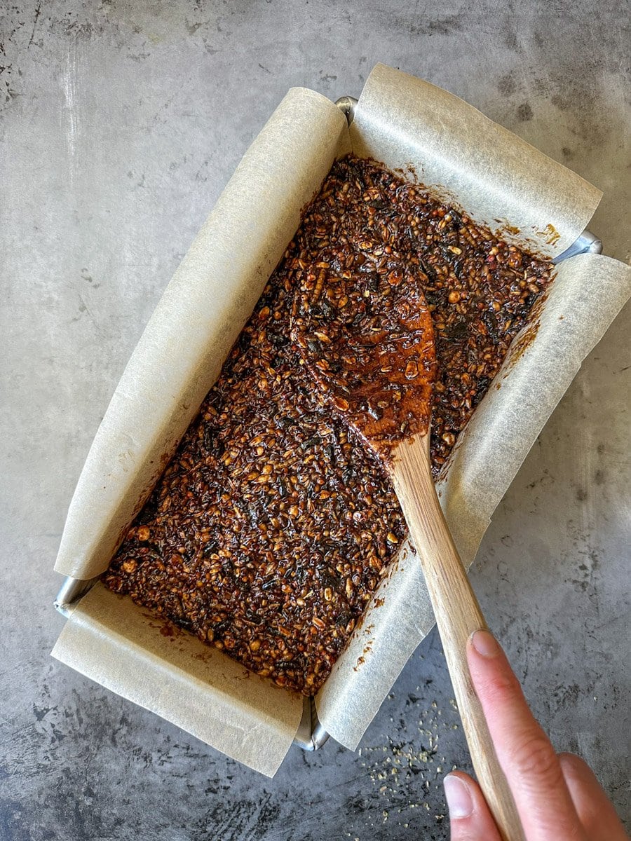 The flock block is being patted down inside of a bread pan lined with parchment paper using a wooden spoon to form a solid block.