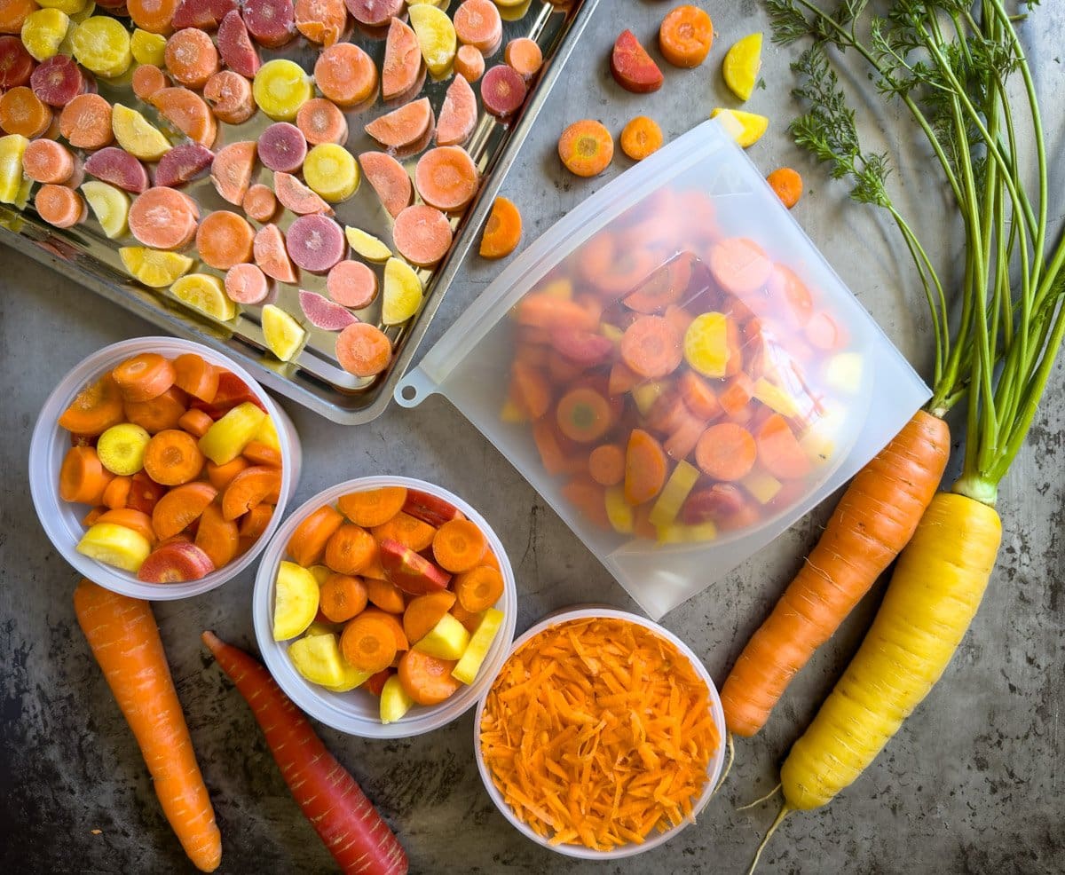 Slice and shredded roots in freezer containers and a silicone bag. Some sliced roots are on a baking sheet that have been frozen. 