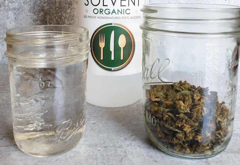 A half pint mason jar is on the left filled with ethyl alcohol, to the right is a pint mason jar with 8 grams of decarbed cannabis in it, behind and in between the two mason jars is a quart bottle of 200 proof ethyl alcohol.