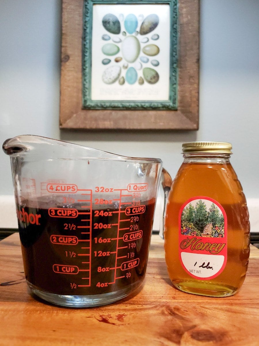 A four cup liquid measuring cup is full to the three cup line with elderberry juice. A jar of honey sits next to it to eventually make elderberry syrup.