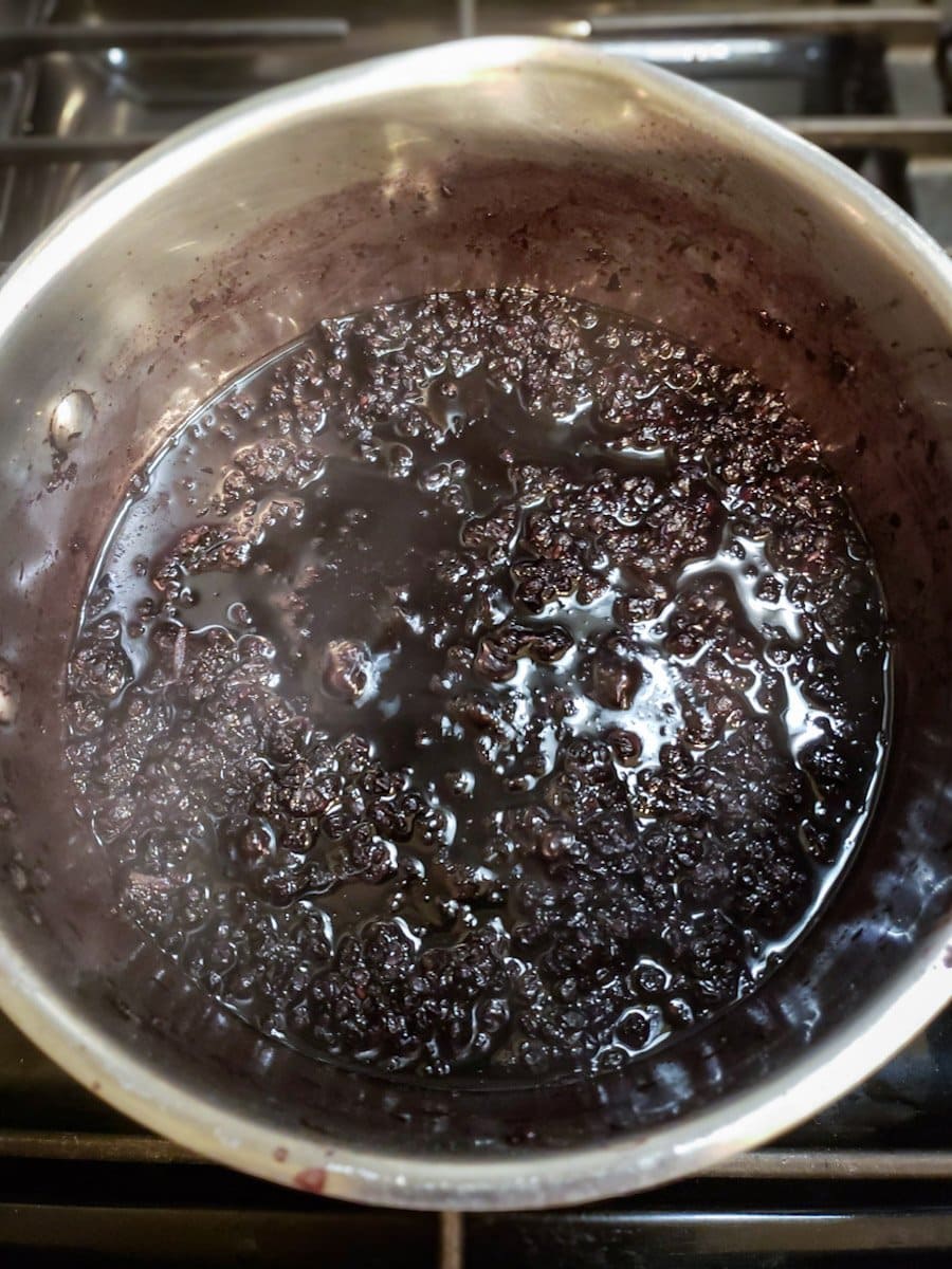A metal pot with simmering dried berries and water that has reduced by a half from the original volume.