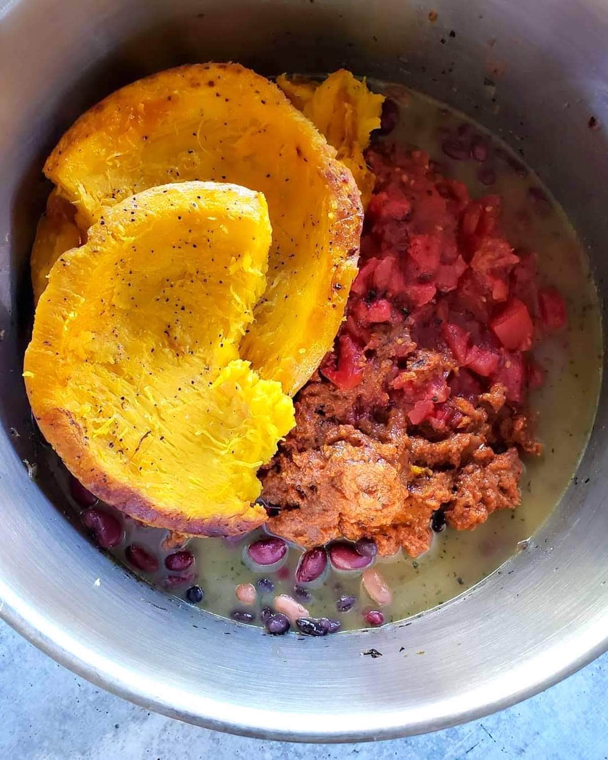 A close up inside the top of the cooking pot, where now the broth, tomatoes, beans, and large chunks of roasted pumpkin have been added