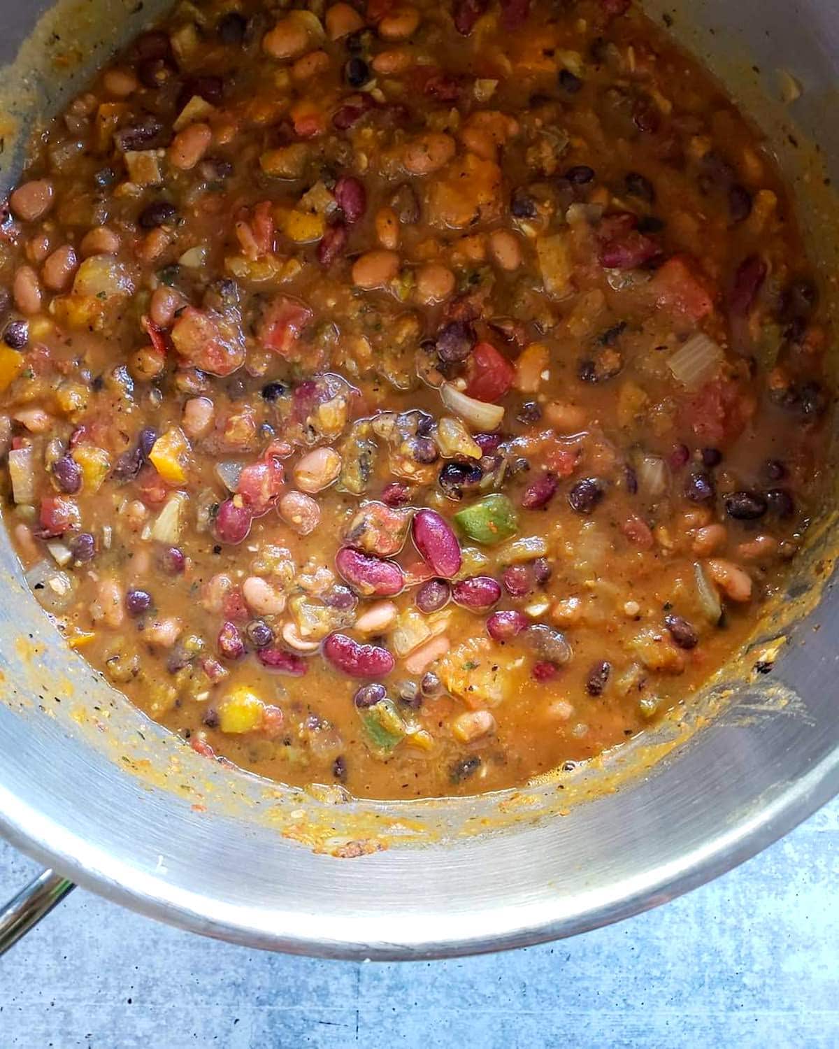 A close up inside the top of the cooking pot with the finished vegetarian pumpkin chili once it has been stirred together and mixed well. You can see each type of bean, onions, peppers, tomato and parts of pumpkin.