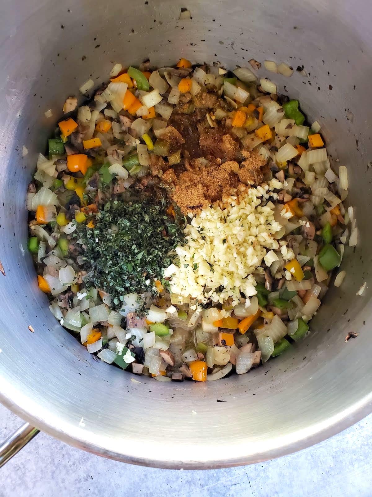 A close up inside a large stainless steel pot, showing the cooked vegetables now with fresh oregano, garlic, and seasonings have also been added to the top