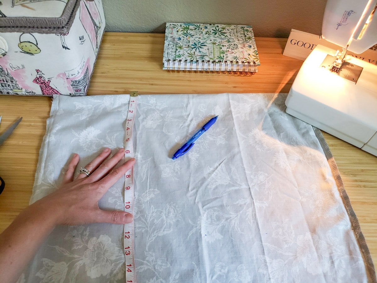 An inside out pillowcase laid on a table, with a sewing machine next to it and a hand holding a measuring tape over the fabric
