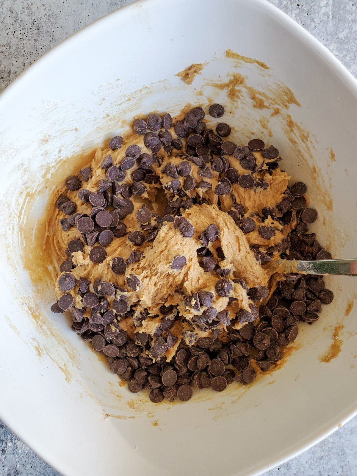 A top view of a white ceramic bowl with the wet and dry cookie dough ingredients mixed together, including chunky chocolate chips.