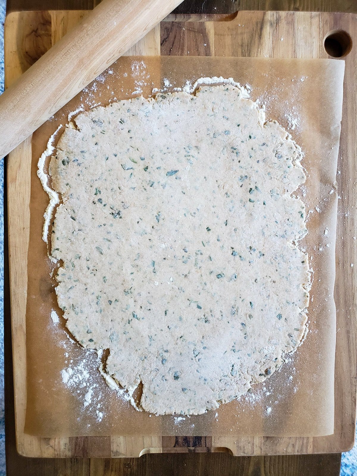 A thinly rolled out piece of dough is on a piece of parchment paper with a wooden rolling pin sitting nearby. 