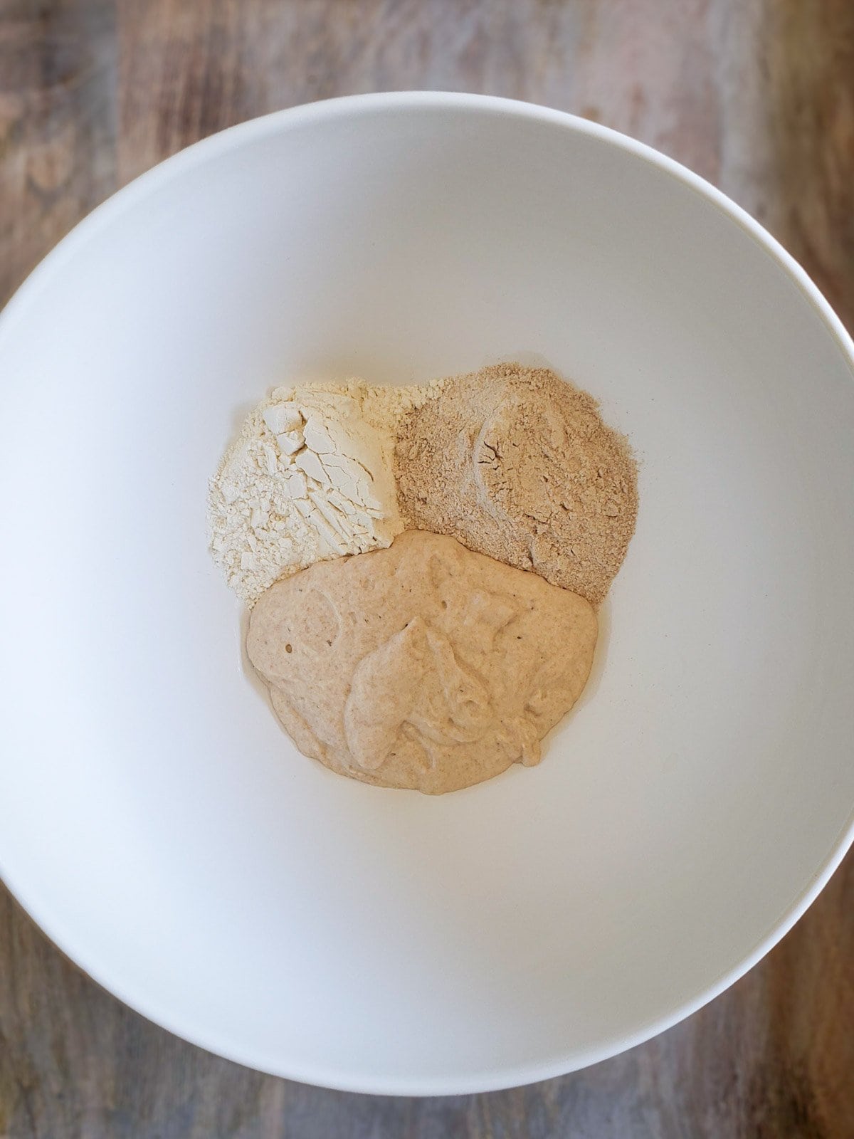 Two types of flour and fresh sourdough starter are inside a large white bowl. 
