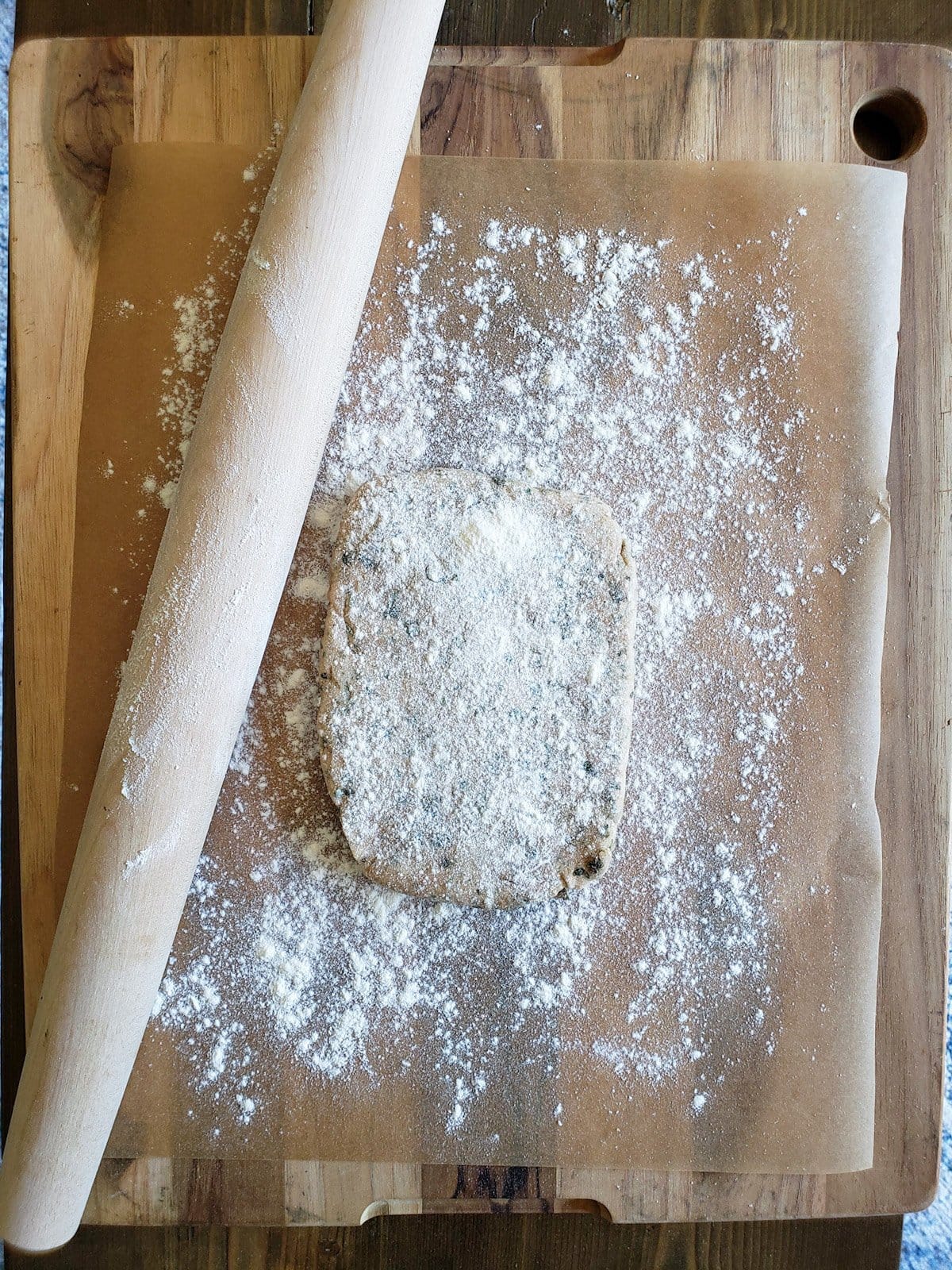 A small rectangle of dough is sitting on parchment paper, it has been dusted with fresh flour and a rolling pin sits next to it. 