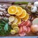 Slices of oranges, lemon, and grapefruit along with whole onion, garlic, ginger, and fresh herbs are on a wood cutting board.