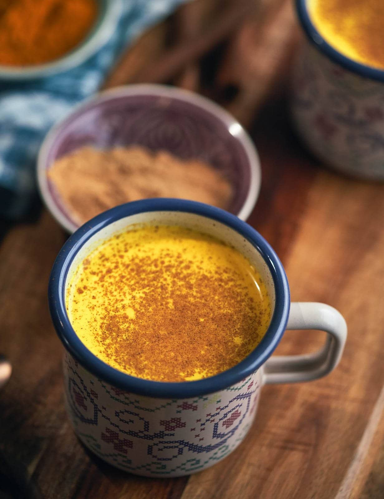 A decorative mug is full of golden milk and is garnished with a sprinkle of cinnamon powder.