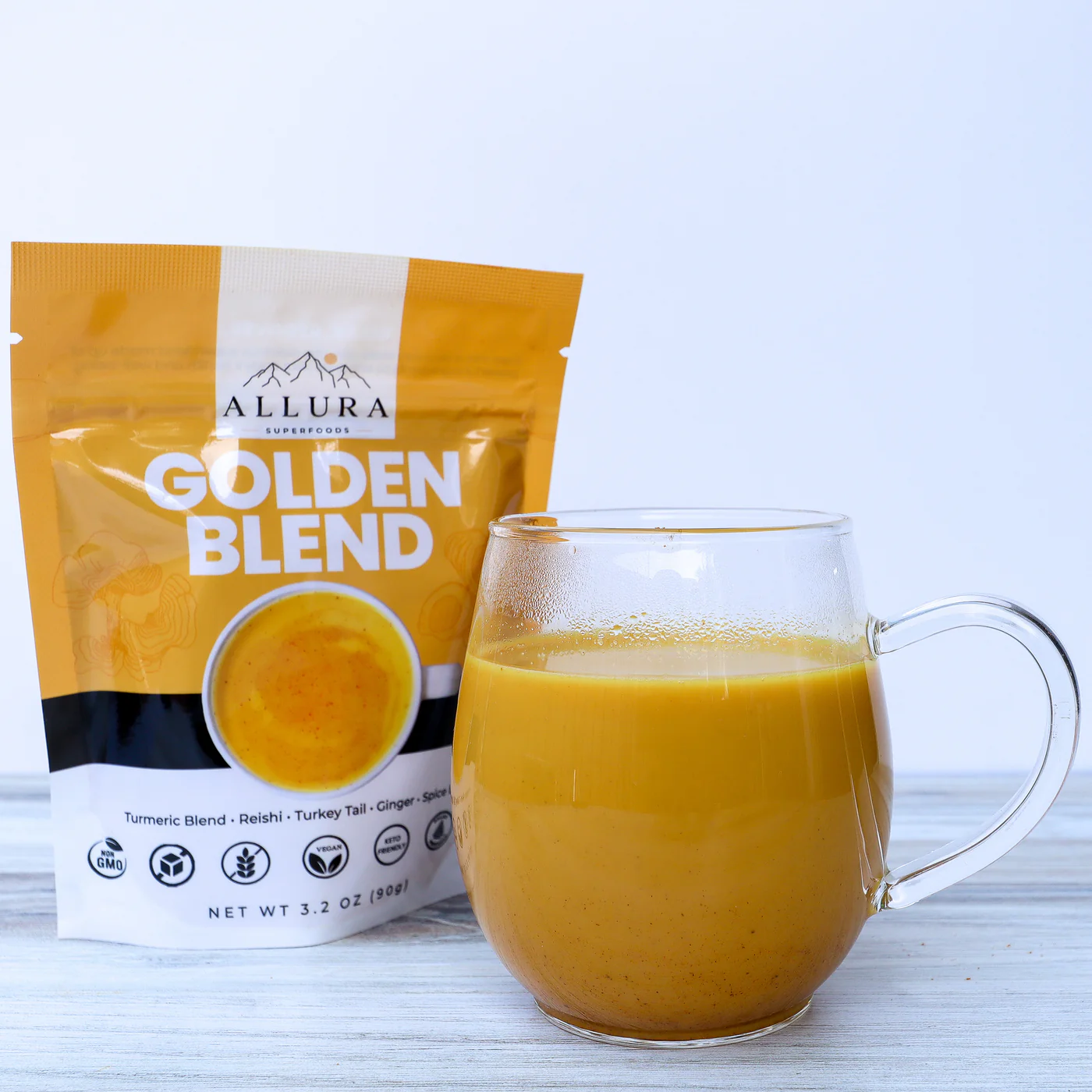 A glass mug with a handle is partially full of golden milk. A bag of Golden Blend (a premade golden milk mix) sits next to it,