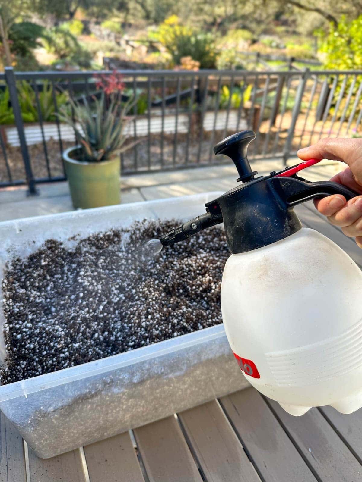 A hand held sprayer is being used to wet diy seed starting mix that is inside of a large tote.