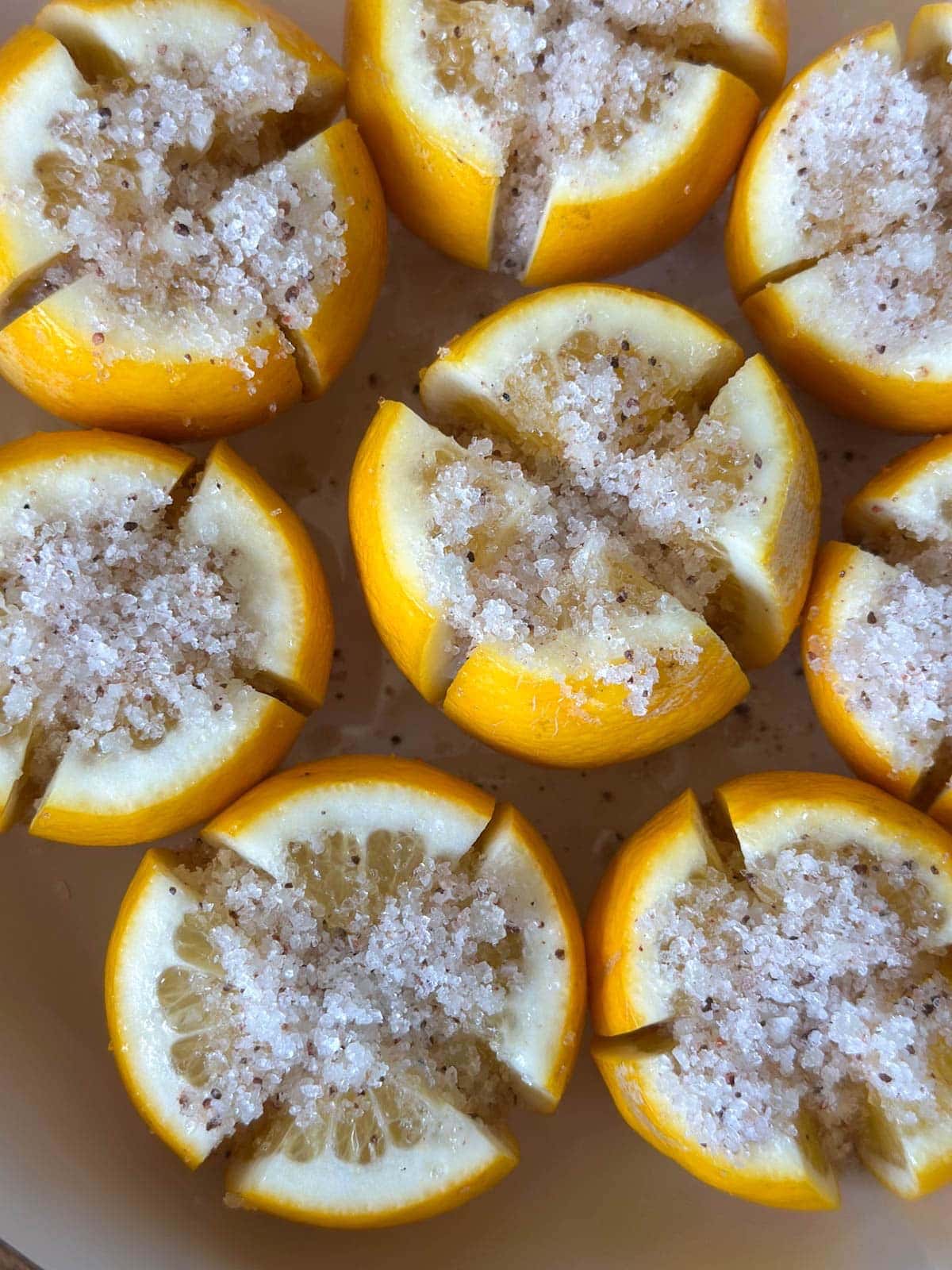 Citrus that has been sliced partially through into quarters has alt packed on top of each piece along with salt inside the quarter segments.