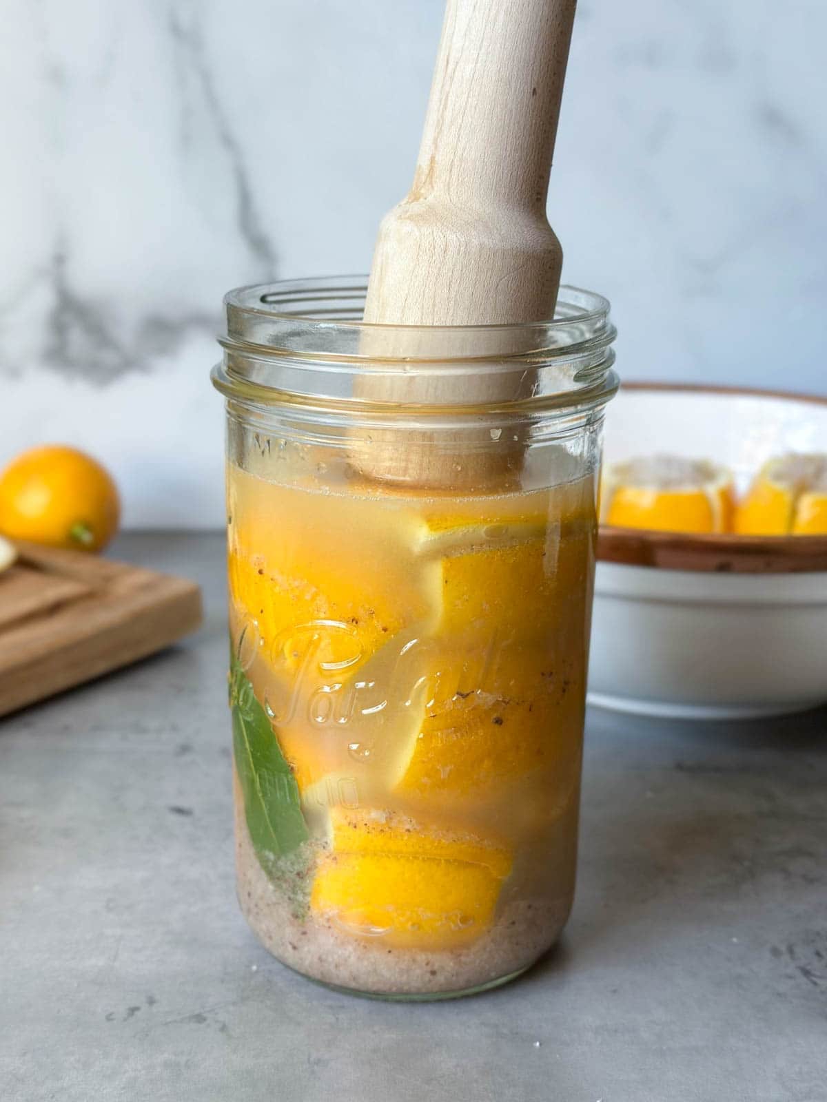A wood pounder is being pressed into a jar packed with lemons, their juices, and salt to make preserved lemons.