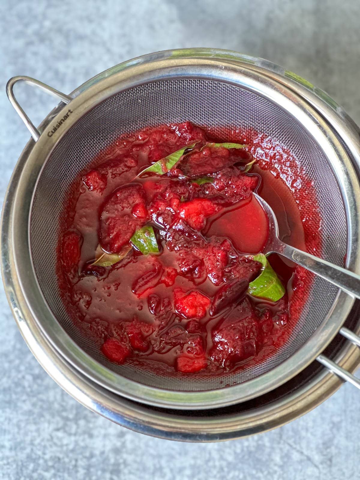 Macerated fruit has just been added to a fine mesh strainer on top of a metal bowl. 