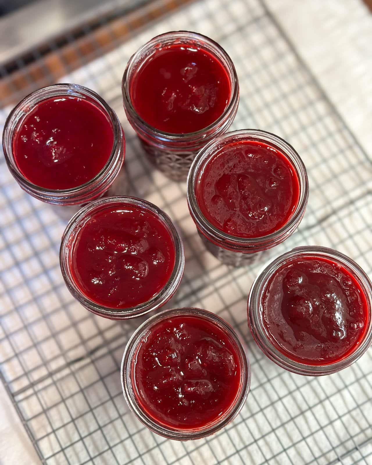 Six half pint mason jars full of plum jam sitting on top of a wire cooling rack.