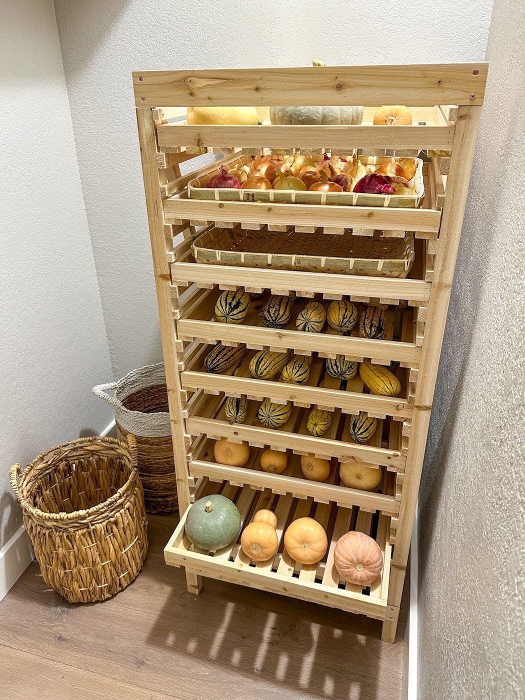 A storage rack made of wood inside of a closet. Each rack has a variety of winter squash and alliums on it.