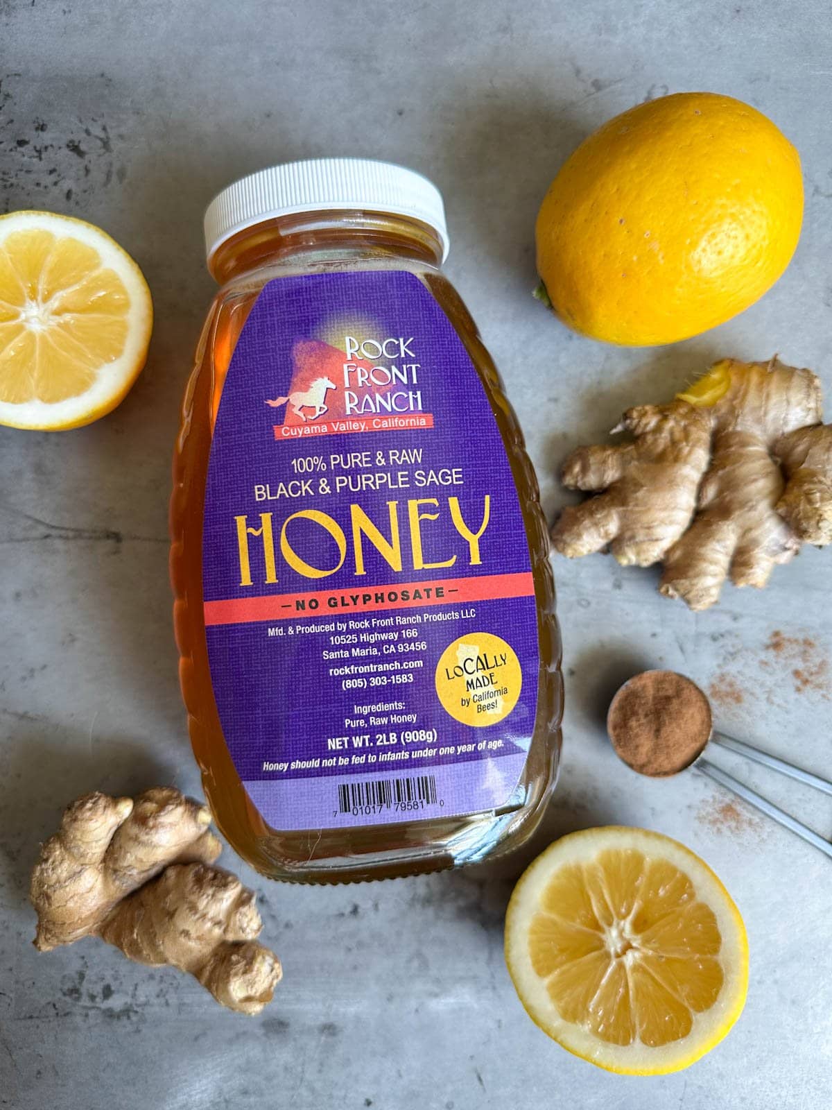 A jar of honey, fresh ginger, whole and halved lemons, and a teaspoonful of cinnamon are scattered about.