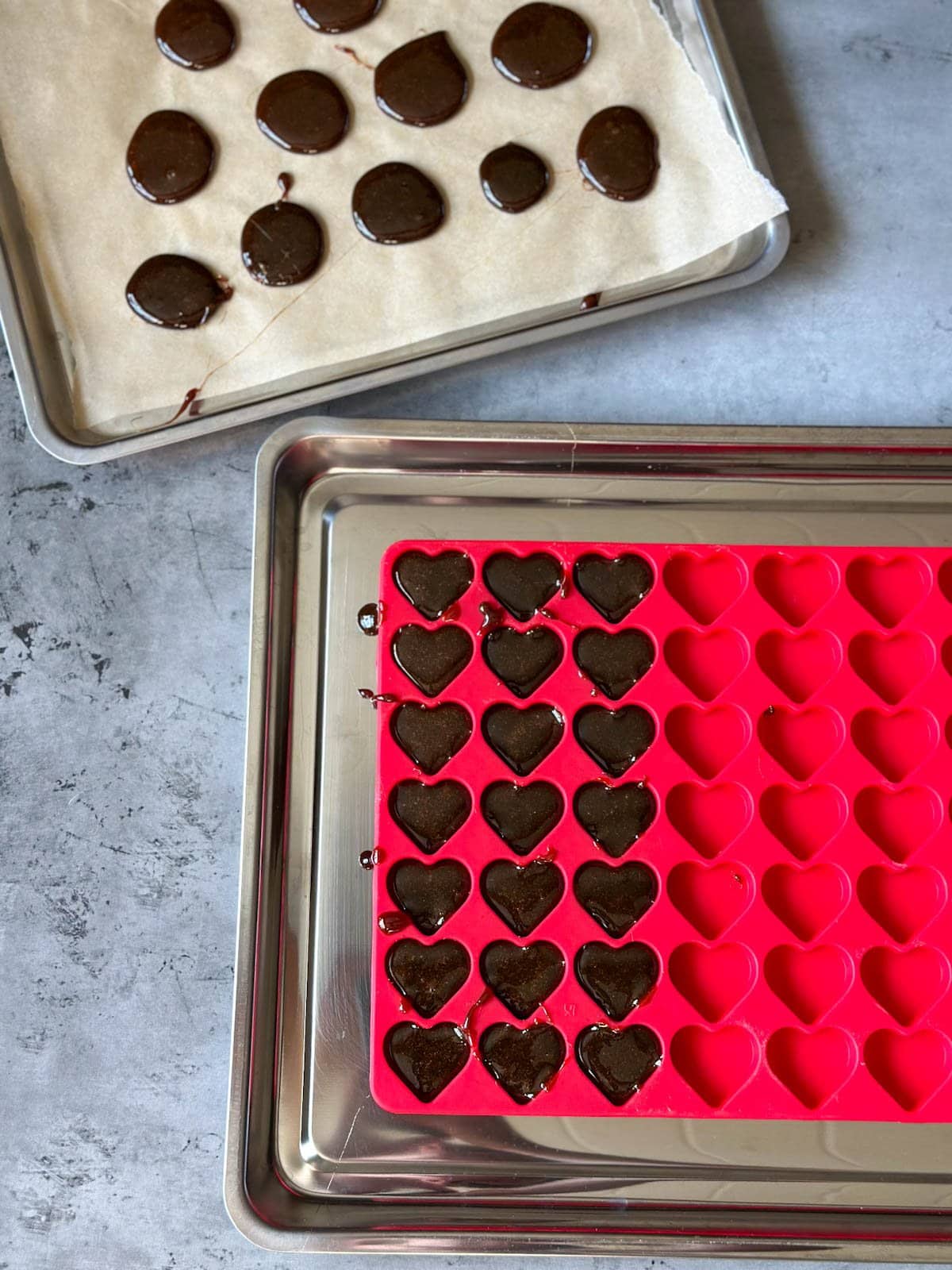 A heart mold tray is partially filled with the homemade cough drop mixture, a sheet of parchment paper is above it with dollops of the mixture in the shape of discs.
