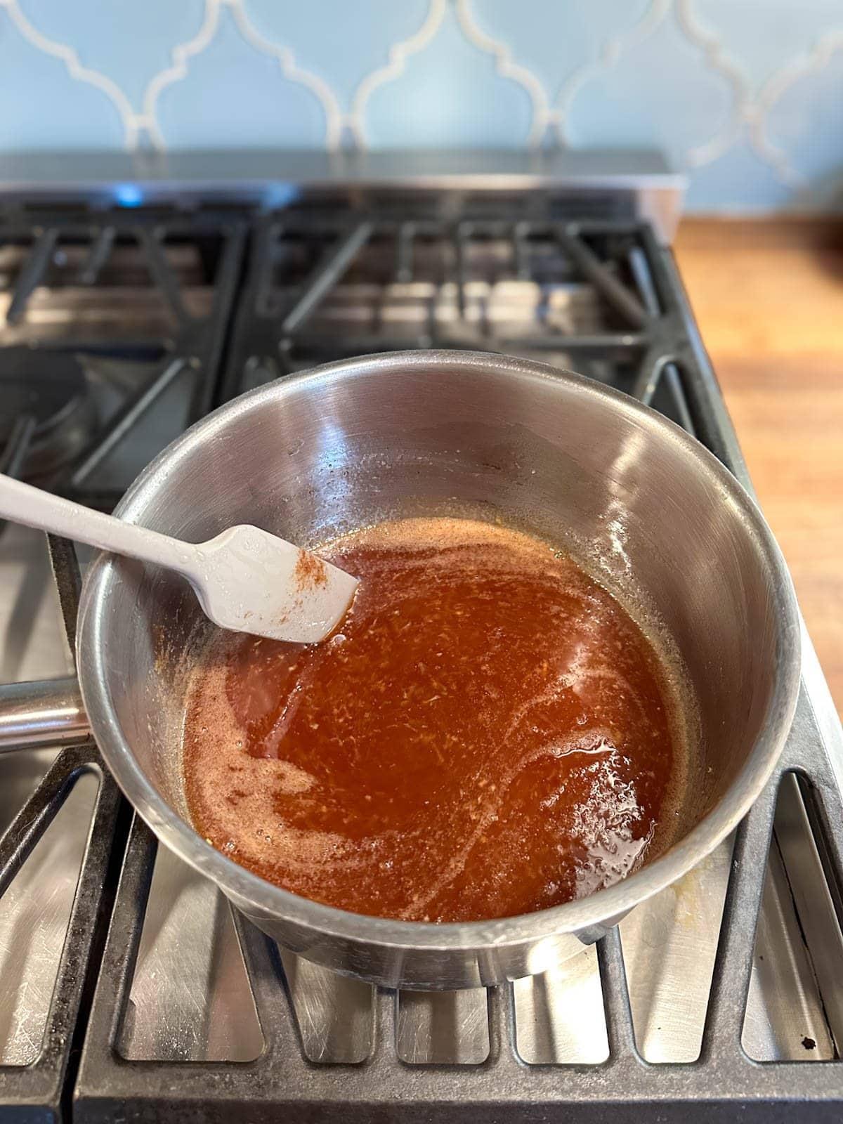 A sauce pan partially full of a mixture that is light brown in color with a small amount of bubbles forming on the surface.
