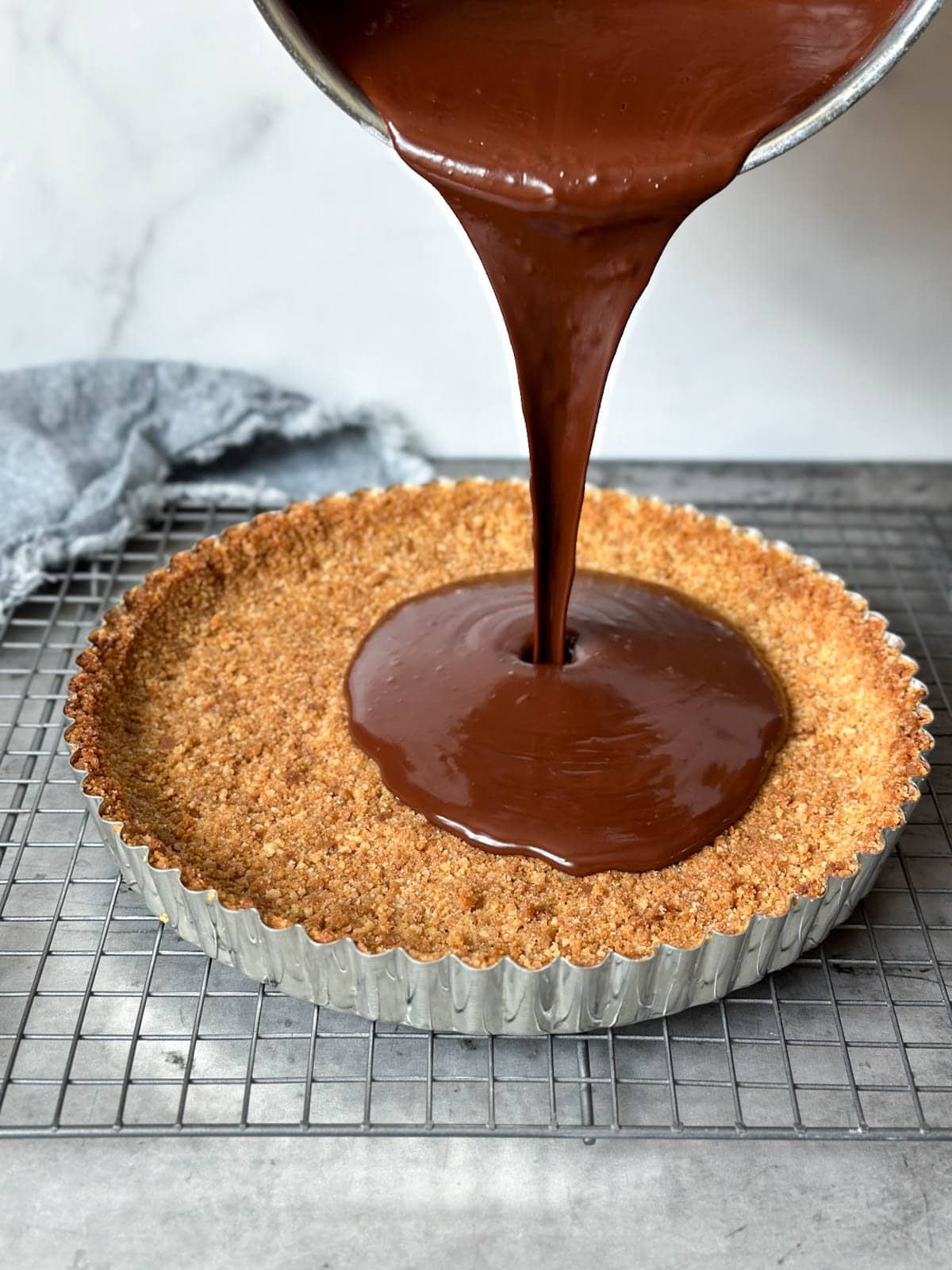 A melted mixture being poured into a graham cracker crust lined metal pie dish.