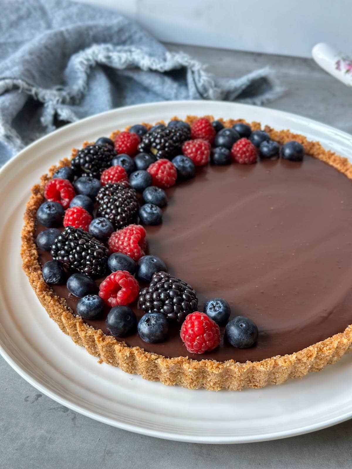 Blackberries, blueberries, and raspberries are arranged in a half crescent moon shape on top of a pie with graham cracker crust.