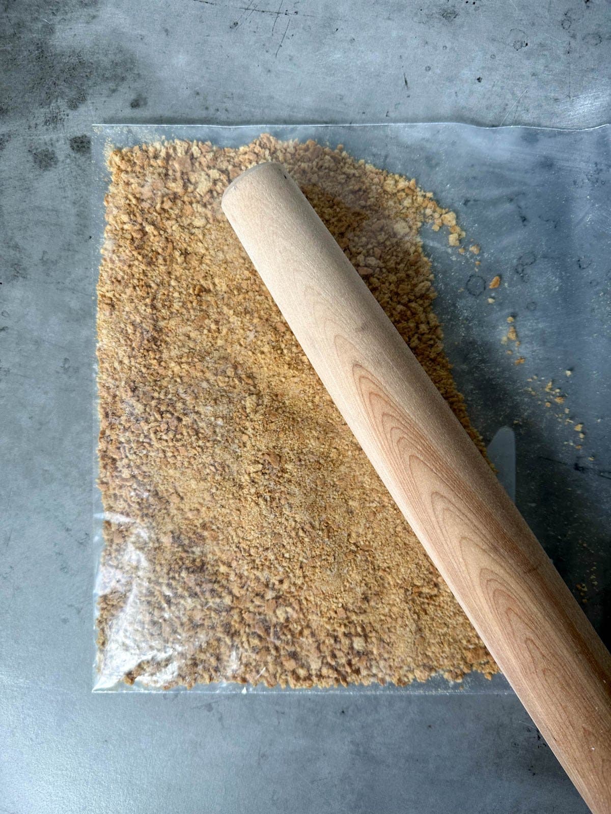A bag of graham cracker crumbs has a wooden rolling pin resting on top of it.