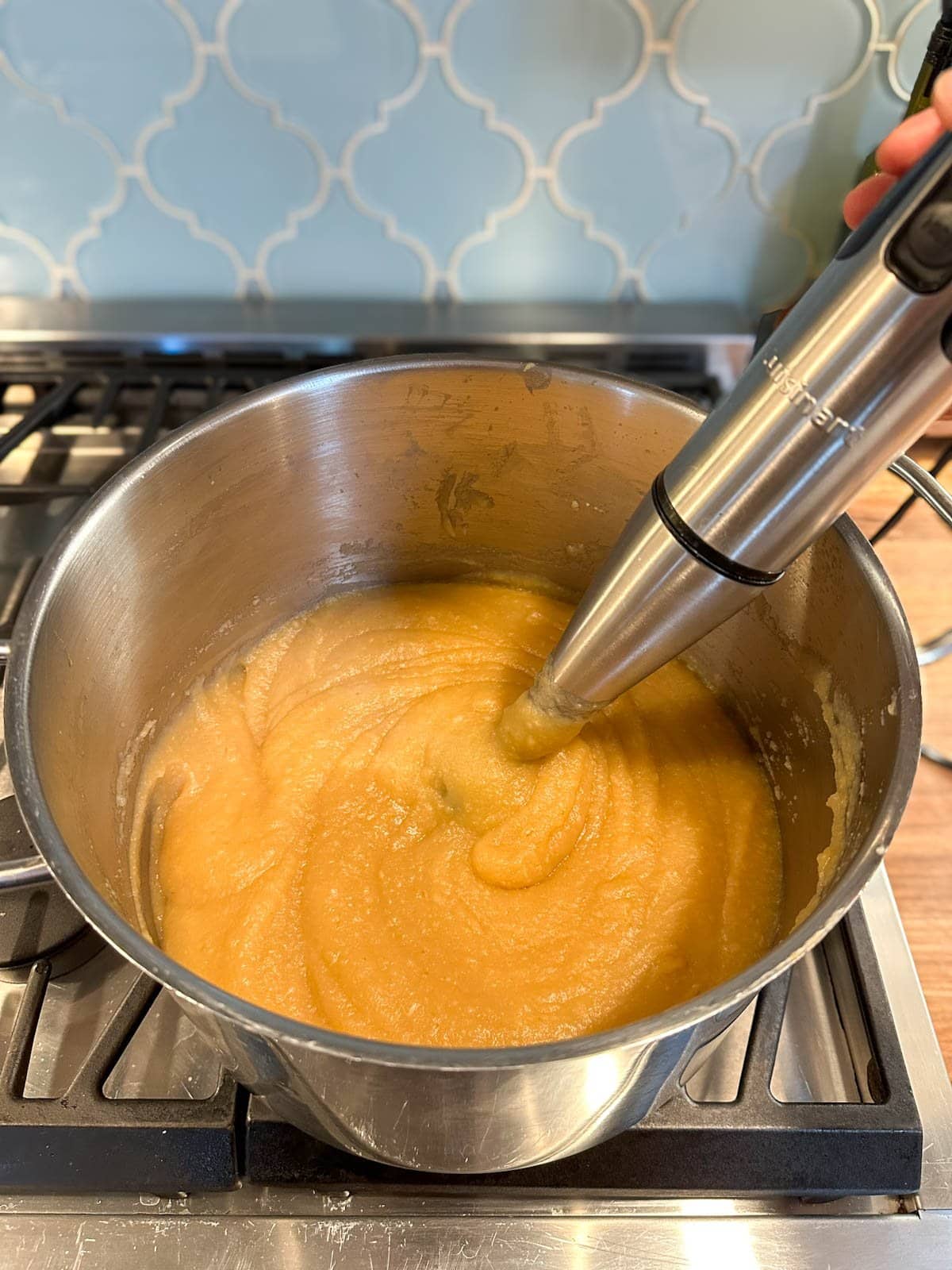 An immersion blender sits inside of a stock pot as it blends the contents smooth.