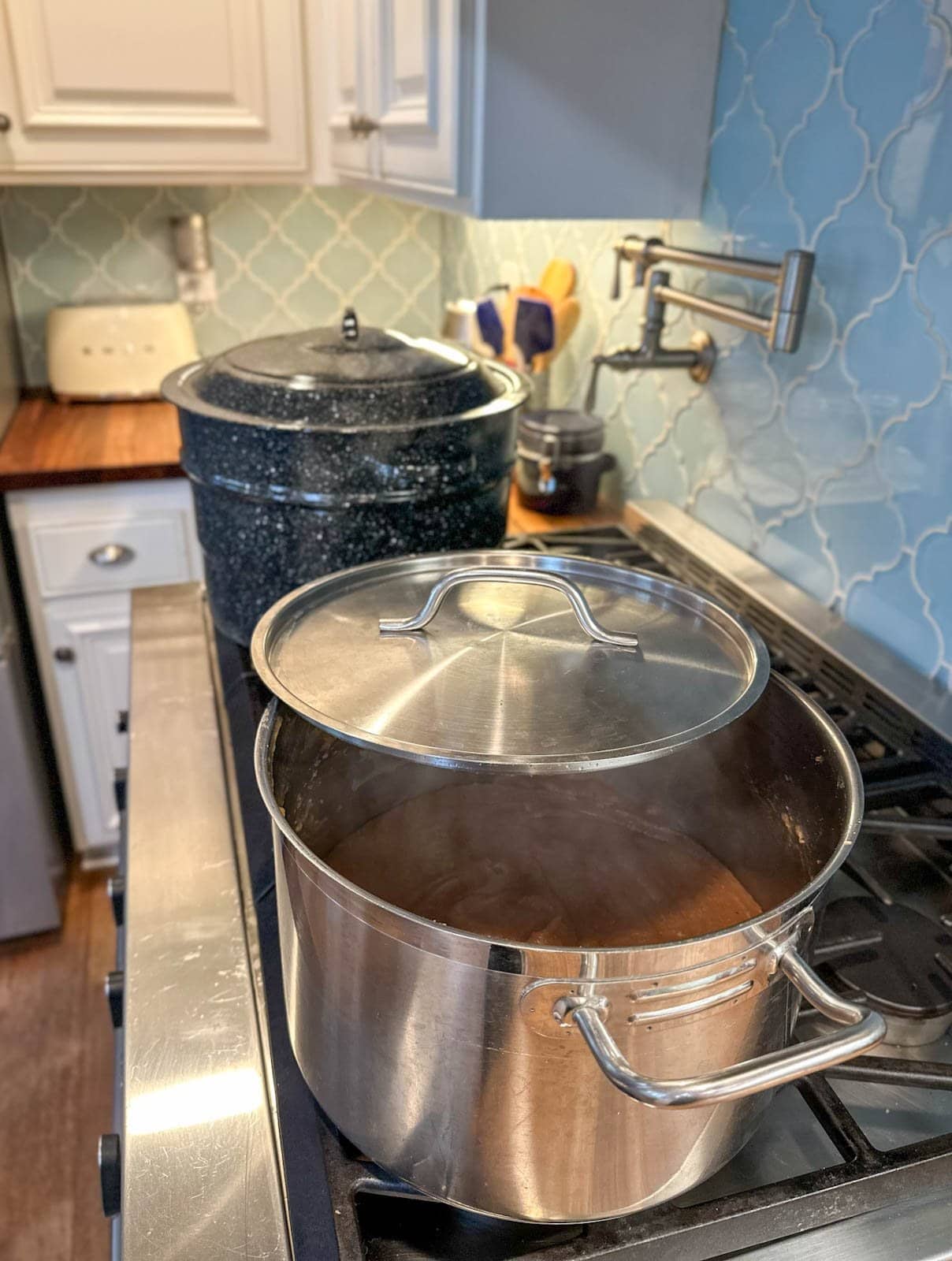 A stock pot of apple butter is reducing on the stove top while a canning pot sits just beyond.