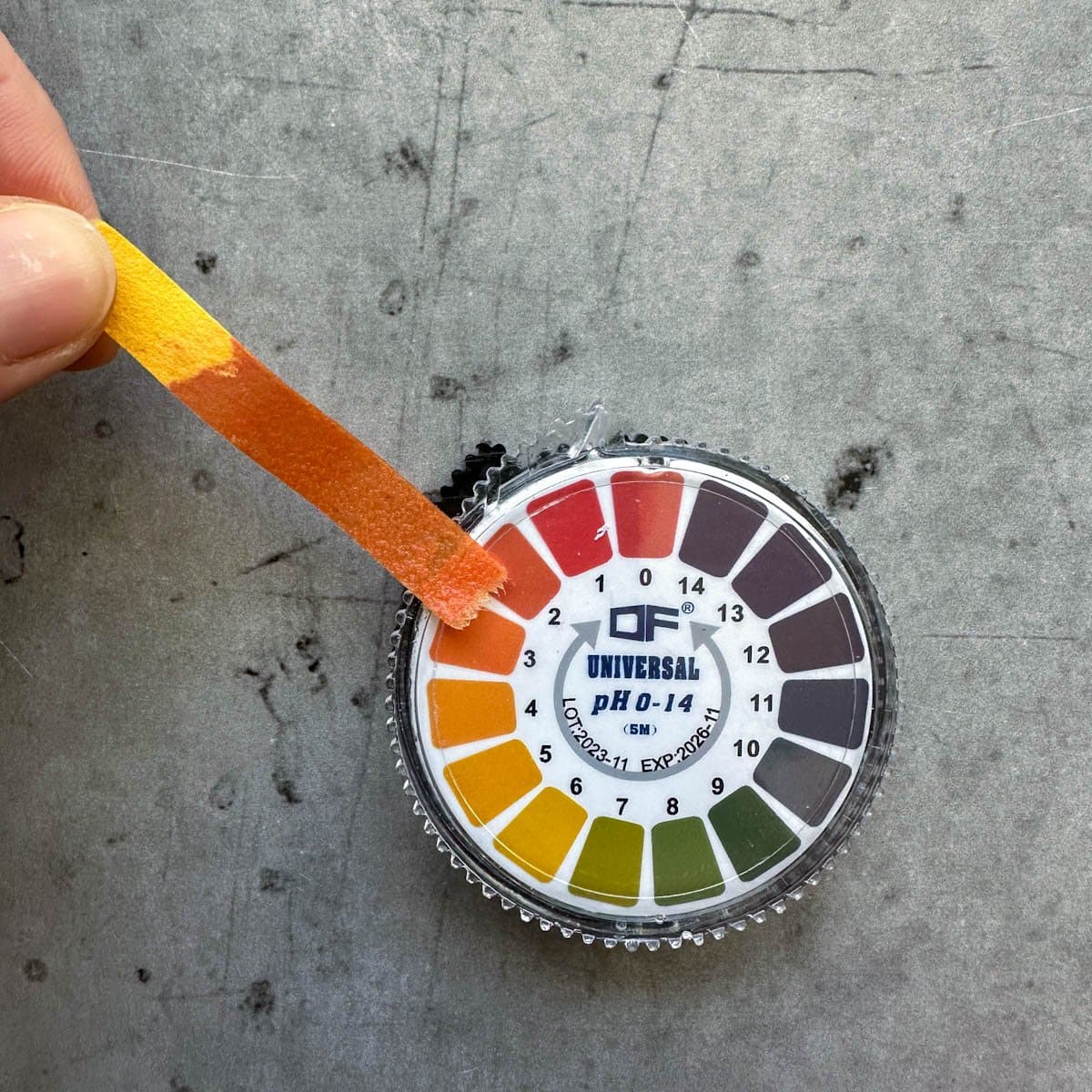A used pH test strip rests next to the corresponding color of the pH test chart.