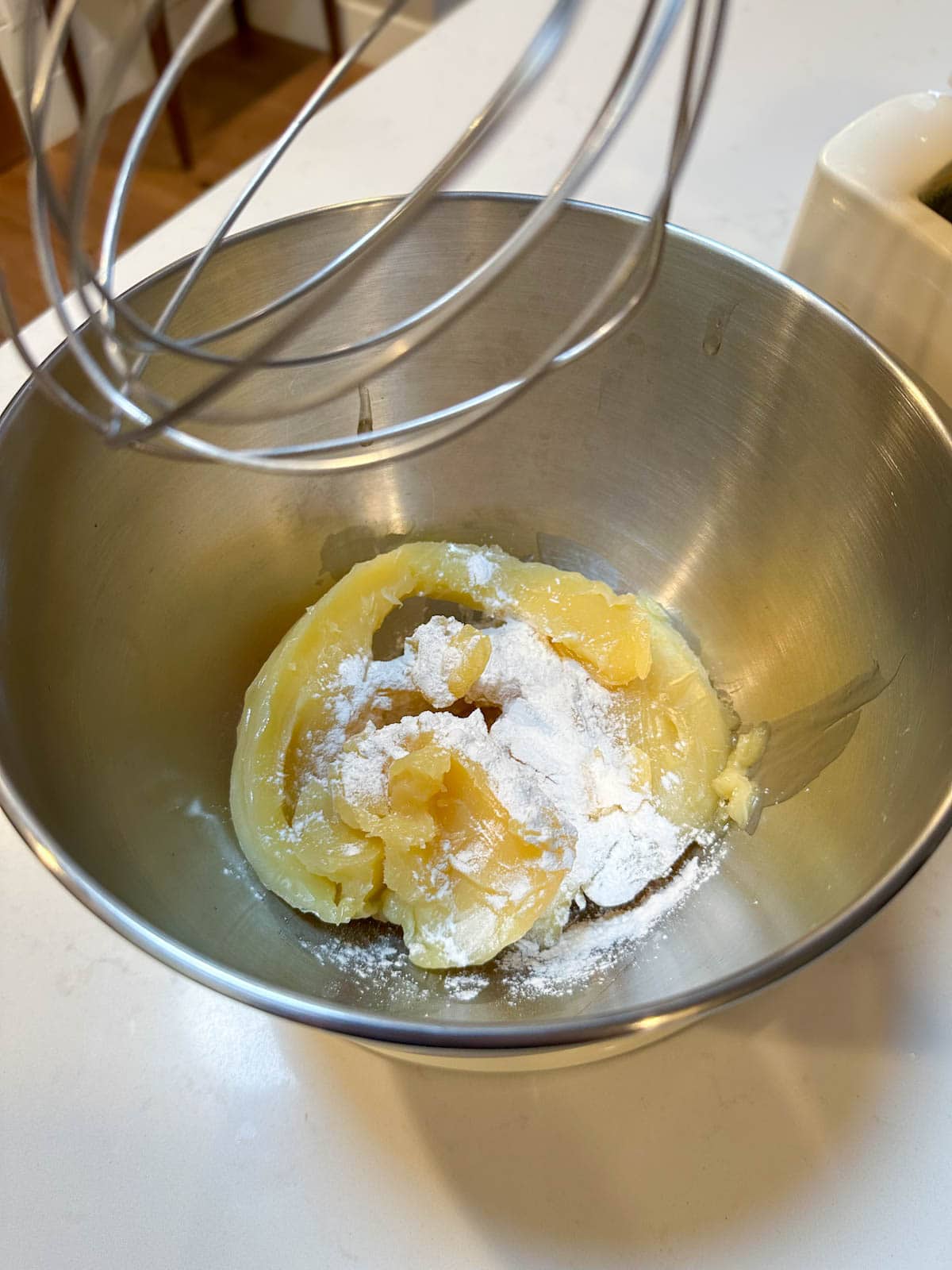 A close up inside a stainless steel stand mixer (kitchen aid) bowl with the yellow body butter mixture inside, plus white arrowroot powder on top - not yet whipped