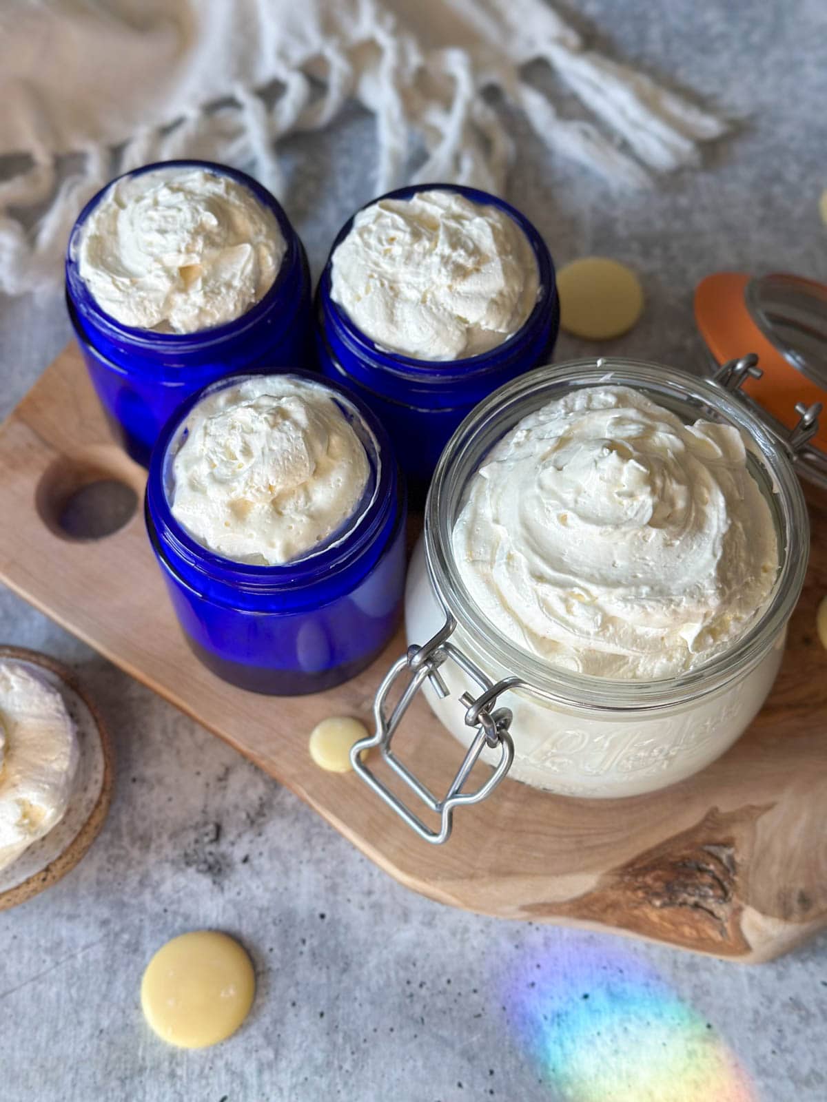 Looking down on a pint-size glass jar with a flip top alongside 3 smaller 4-ounce blue glass jars, all full of fluffy whipped body butter swirled to the top