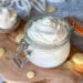 A close up of a Le Parfait 12-ounce glass jar with a flip-top lid full of fluffy white whipped body butter, swirled on top. There are also cocoa butter wafters laying around the base of the jar, and a large spoon full of whipped body butter laying off to the side