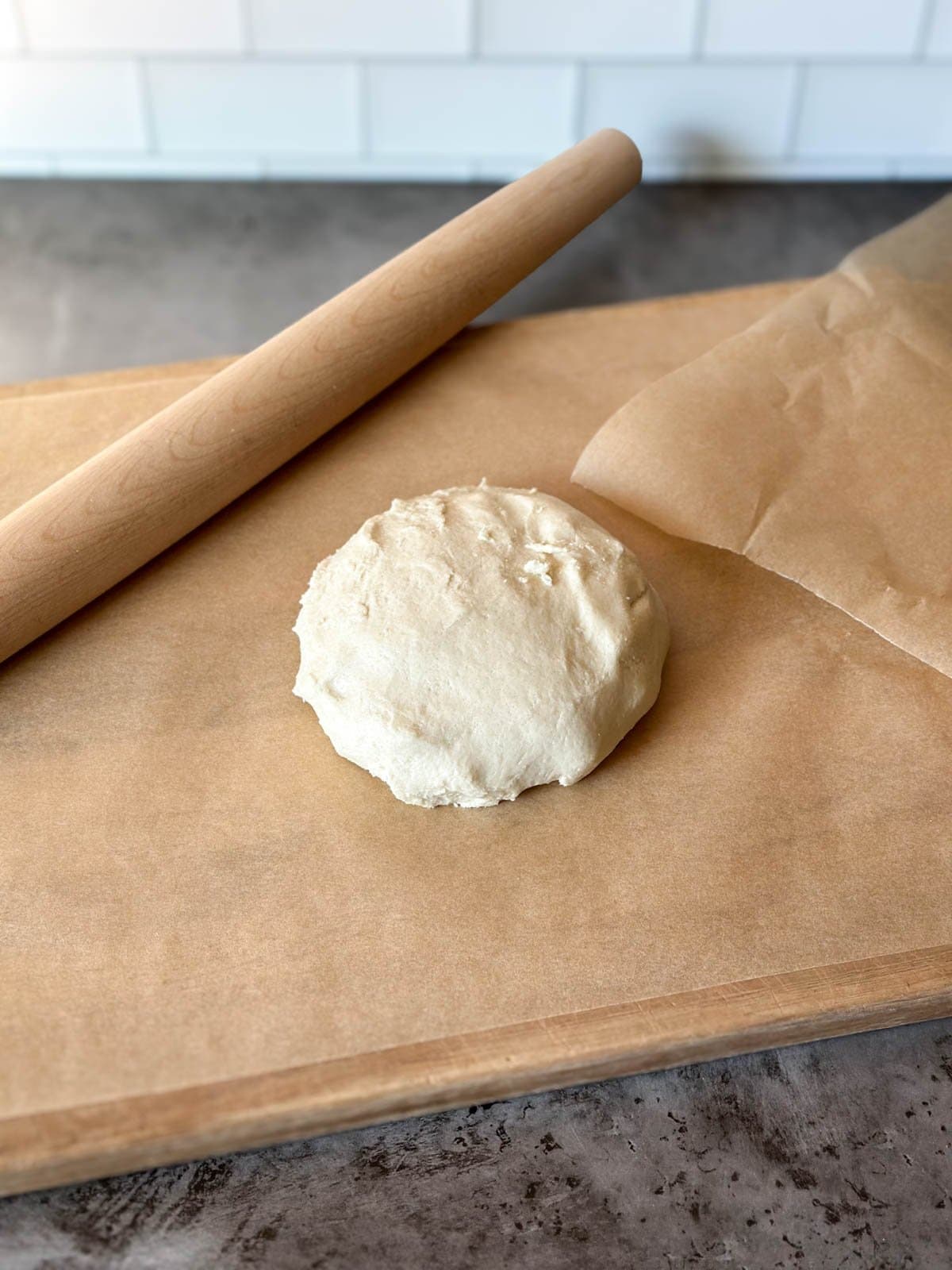 A dough ball sitting on top of a piece of parchment paper with a wooden rolling pin nearby.