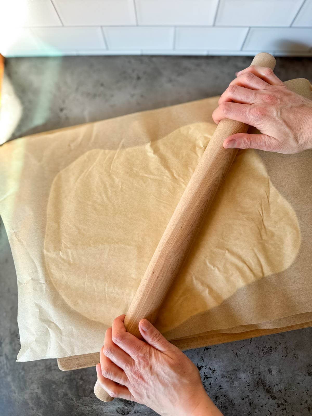 A rolling pin being used to roll out the material sandwiched in between to layers of parchment paper.