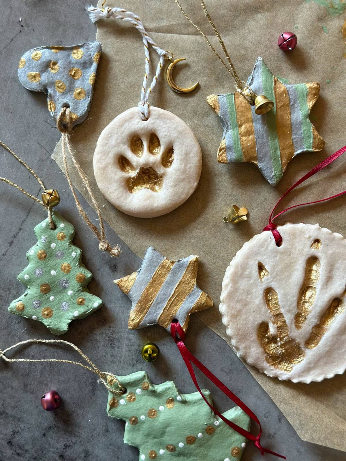 Salt dough ornaments of varying shapes and sizes spread out on a flat surface after they have had the final touches of adding ribbon, bells, and other adornments before hanging on a tree.