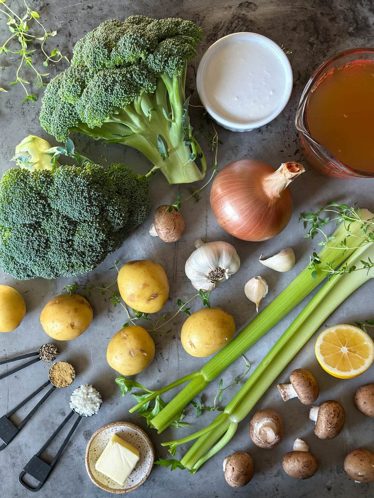 A variety of vegetables, herbs, garlic, onions, coconut milk, broth,  butter and seasonings are scattered about.  