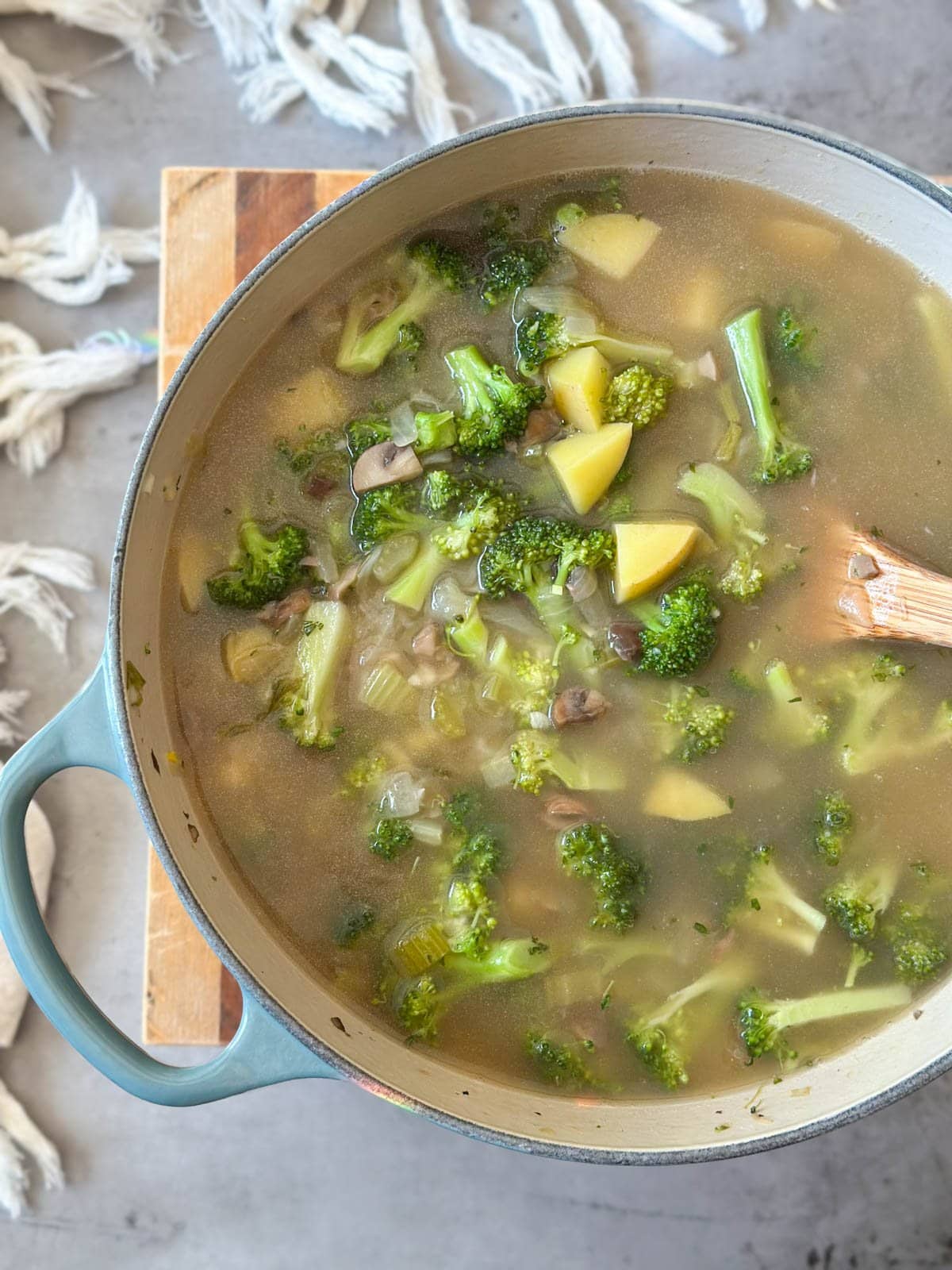 Broccoli, mushrooms, celery, potatoes, and various other ingredients are floating in broth inside of a pot. 