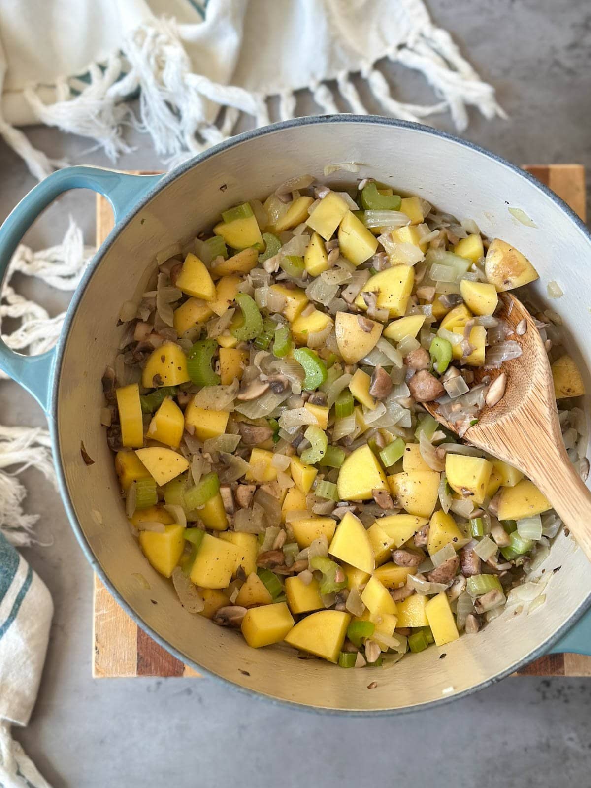 Veggies being sautéed in a pot, a wooden spoon is resting inside the pot as it's used to stir the mixture. 