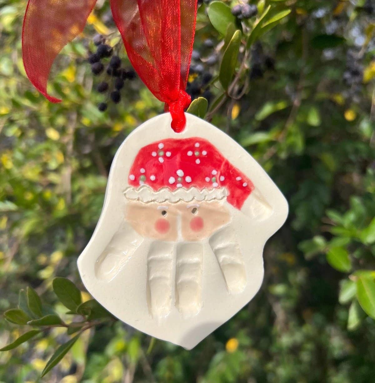 An example of a salt dough ornament where a small child's handprint was turned into a Santa face. The handprint is upside down so the fingers form Santas beard, while the palm makes the face and the thumb is the Santa hat that hangs to the side. The hat is painted red and the face has rosy cheeks