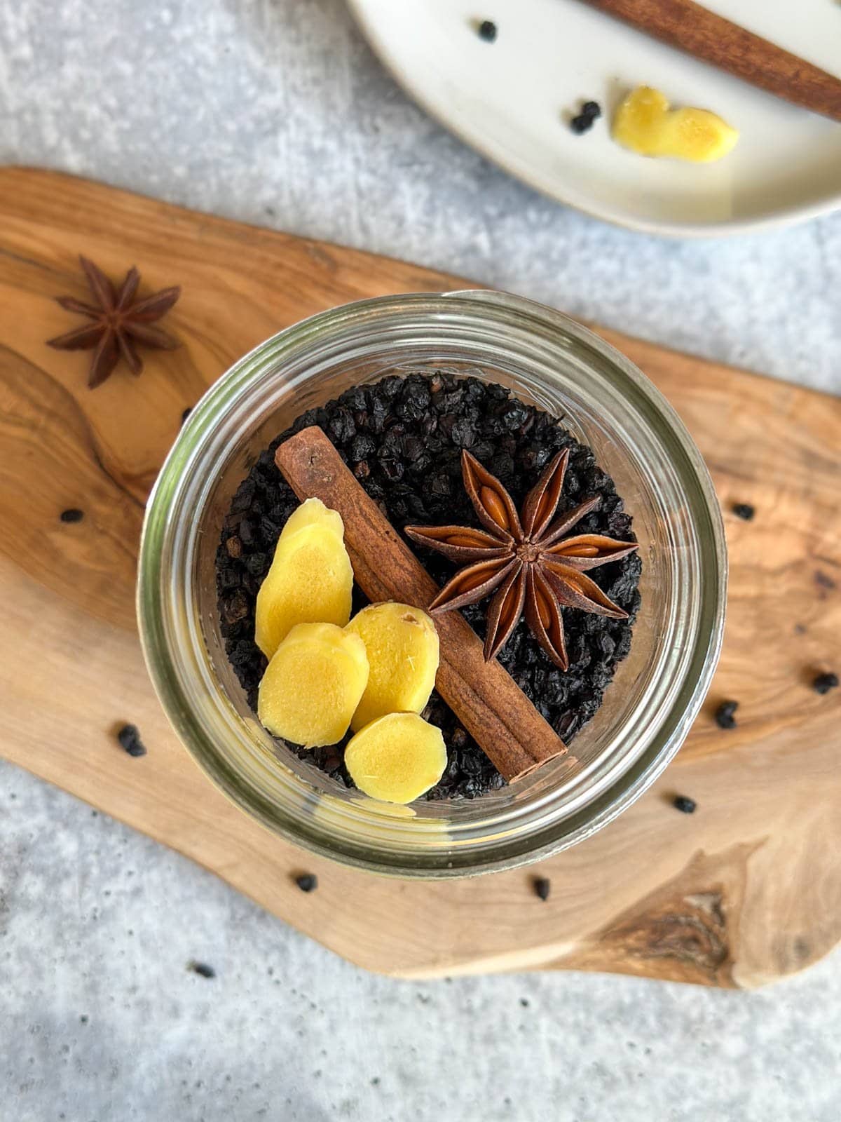 A pint jar is full of dried berries, a cinnamon stick, start anise, and a few slices of fresh ginger.