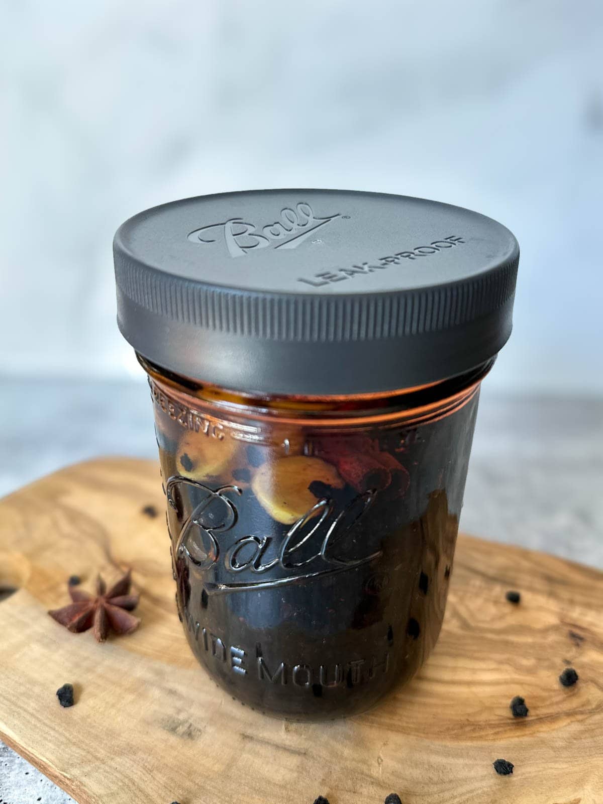 A pint glass mason jar full of dried elderberries, cinnamon stick, star anise, fresh ginger, and alcohol infuse together.