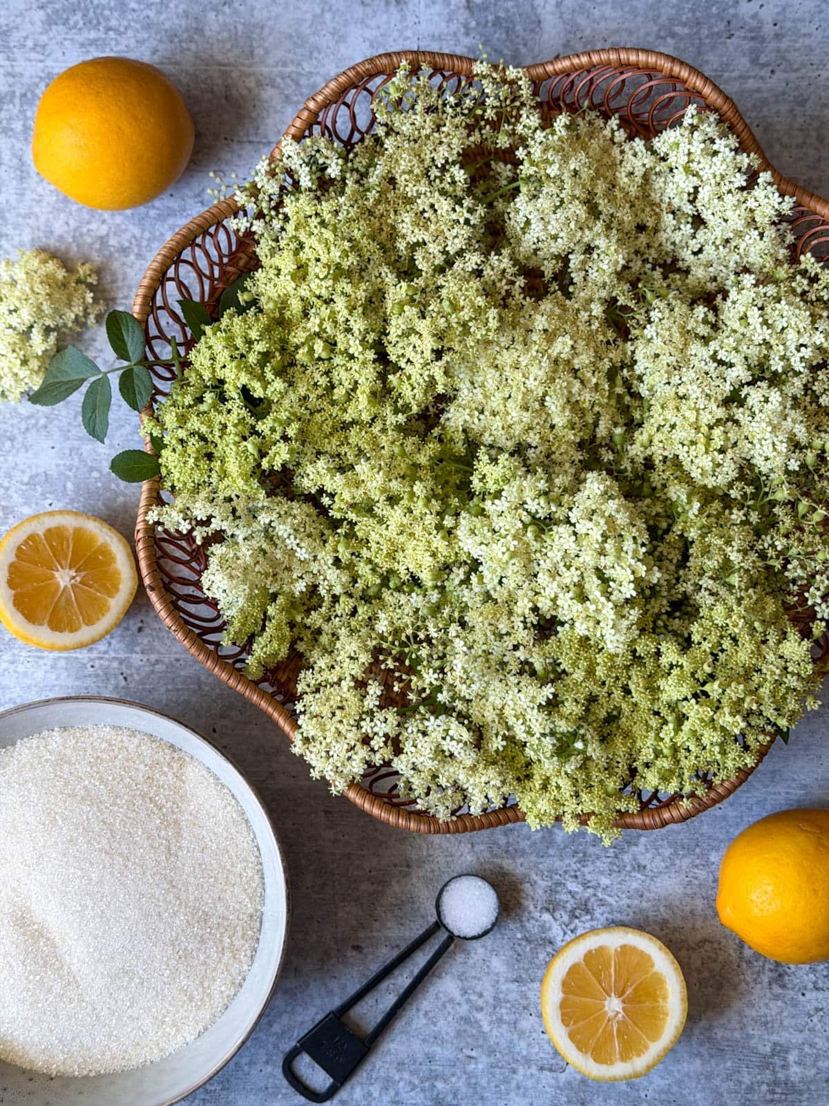 A wicker basket of blooms, full and half lemon sections and a bowl of sugar are arranged in a cluster. 