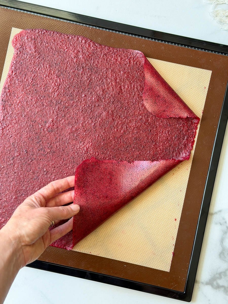 Dried fruit puree is being peeled up by the edges from the silicone mat it was dehydrated on. 