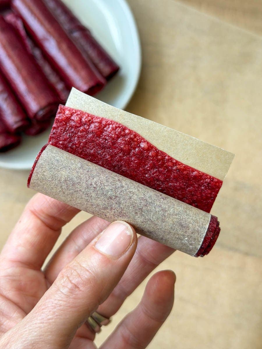 A section of fruit leather rolled together with a small piece of parchment paper creating a "wrapper" for the fruit leather. 